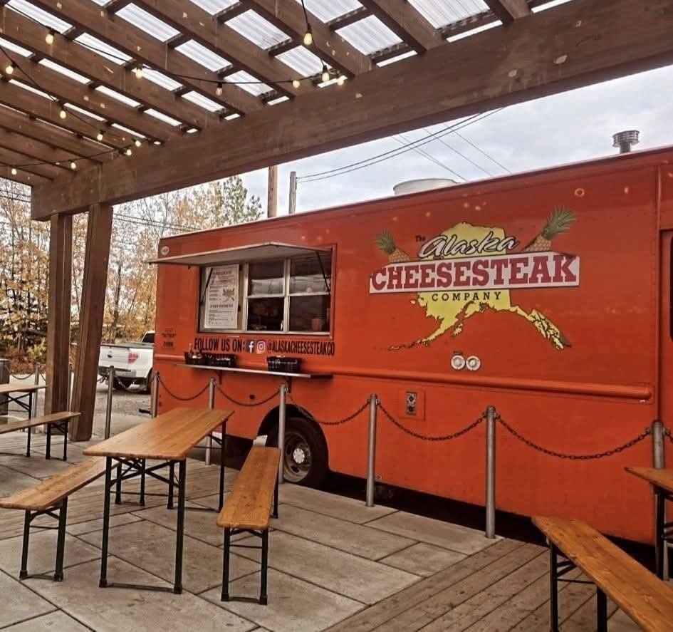 The Alaska Cheesesteak Company food truck parked under string lights with picnic tables