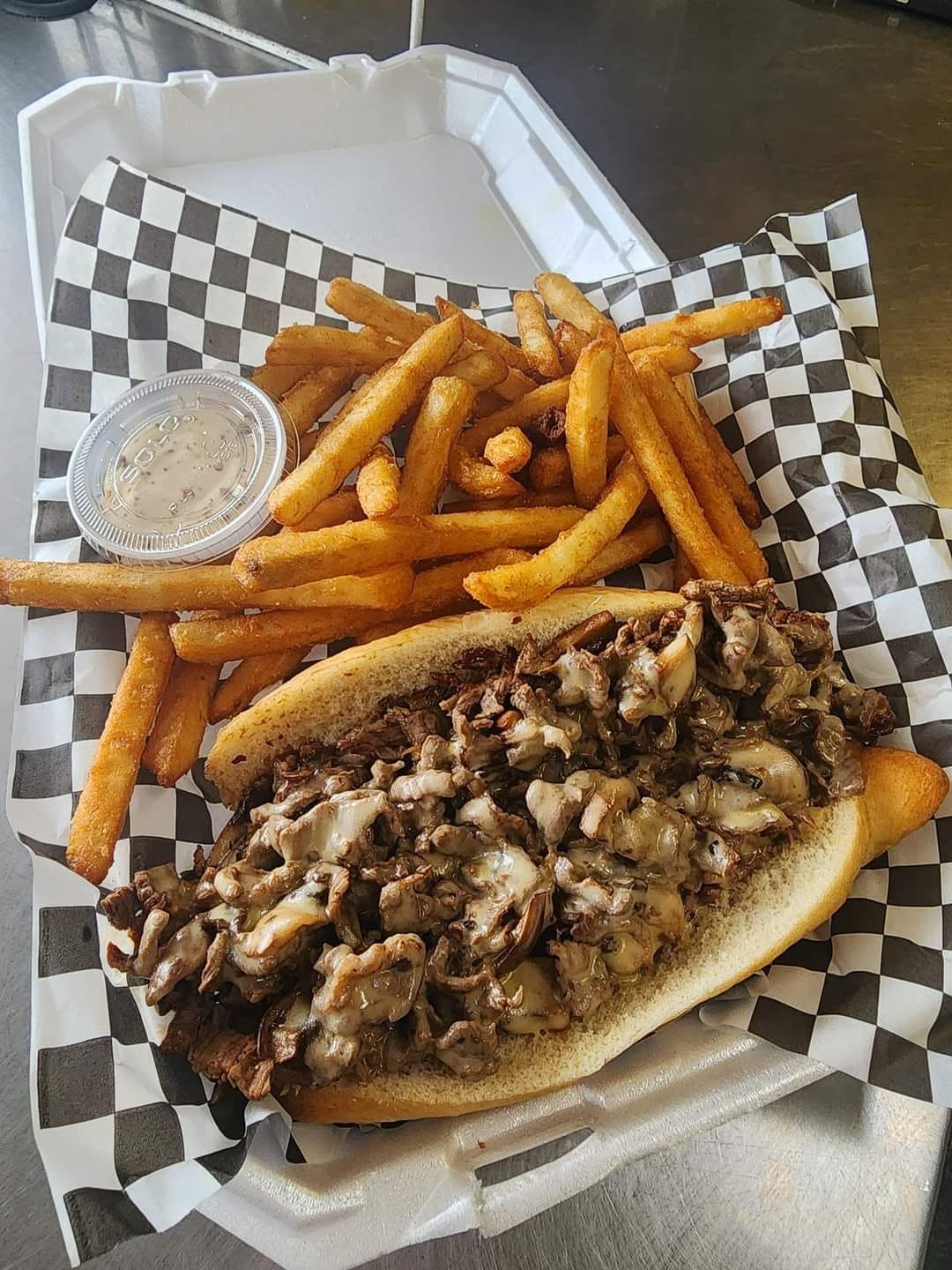 Steak cheesesteak with melted cheese served with a basket of fries